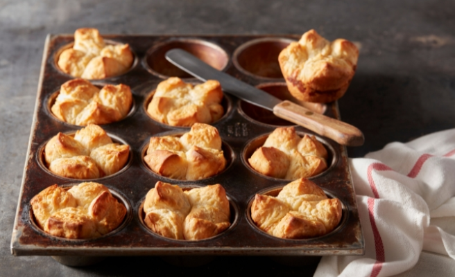 Garlic Parmesan Biscuit Pull-Apart Breads in a muffin tin with spreading spatula and folded white and red towel on the bottom right corner.