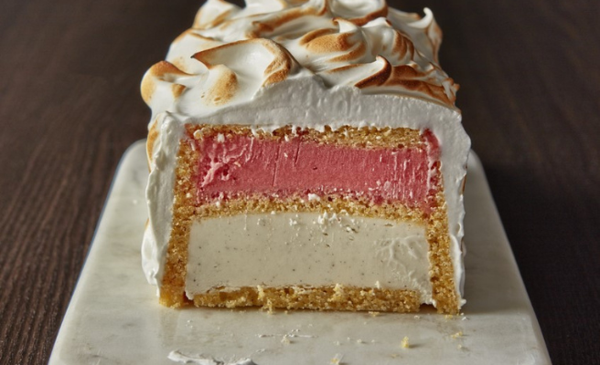 Side view of strawberry shortcake baked Alaska with layers of pink strawberry sorbet, vanilla ice cream and toasted meringue.