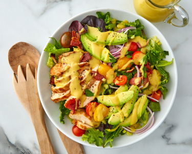 Bowl of fresh salad ontop of marble countertop and wooden serving spoons