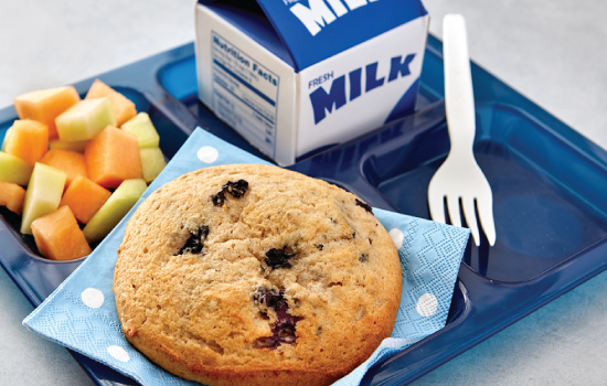 A breakfast plate with a muffin, fresh fruit, and a carton of milk on a blue tray.